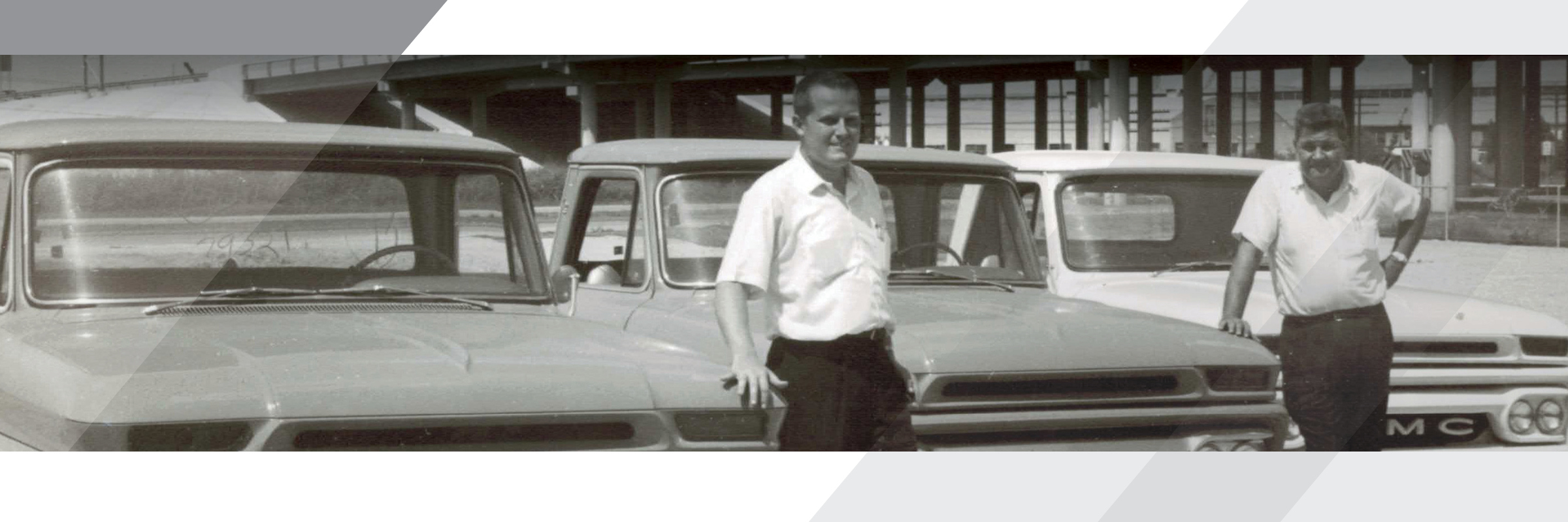 Black and white picture of two men standing in front of cars